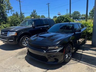 A black Dodge Charger and a black Ford SUV parked side by side in a sunny lot.