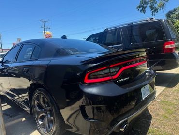 Black Dodge Charger parked next to a black SUV in a sunny outdoor area.