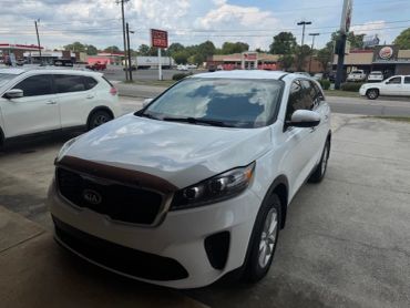 White Kia SUV parked outdoors on a cloudy day.