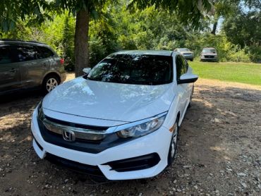 White Honda sedan parked on a gravel area.