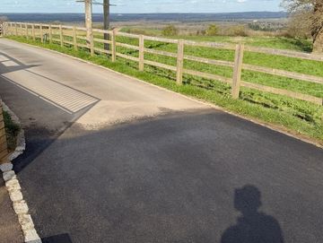 Freshly paved driveway leading to a countryside road with wooden fences.