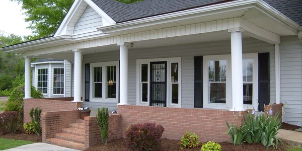 Front porch of a house with white columns and brick base.