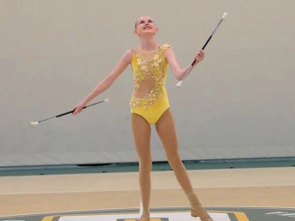 Young baton twirler in a yellow costume performing indoors.