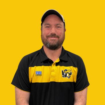 Man smiling wearing a black and yellow sports shirt and cap.