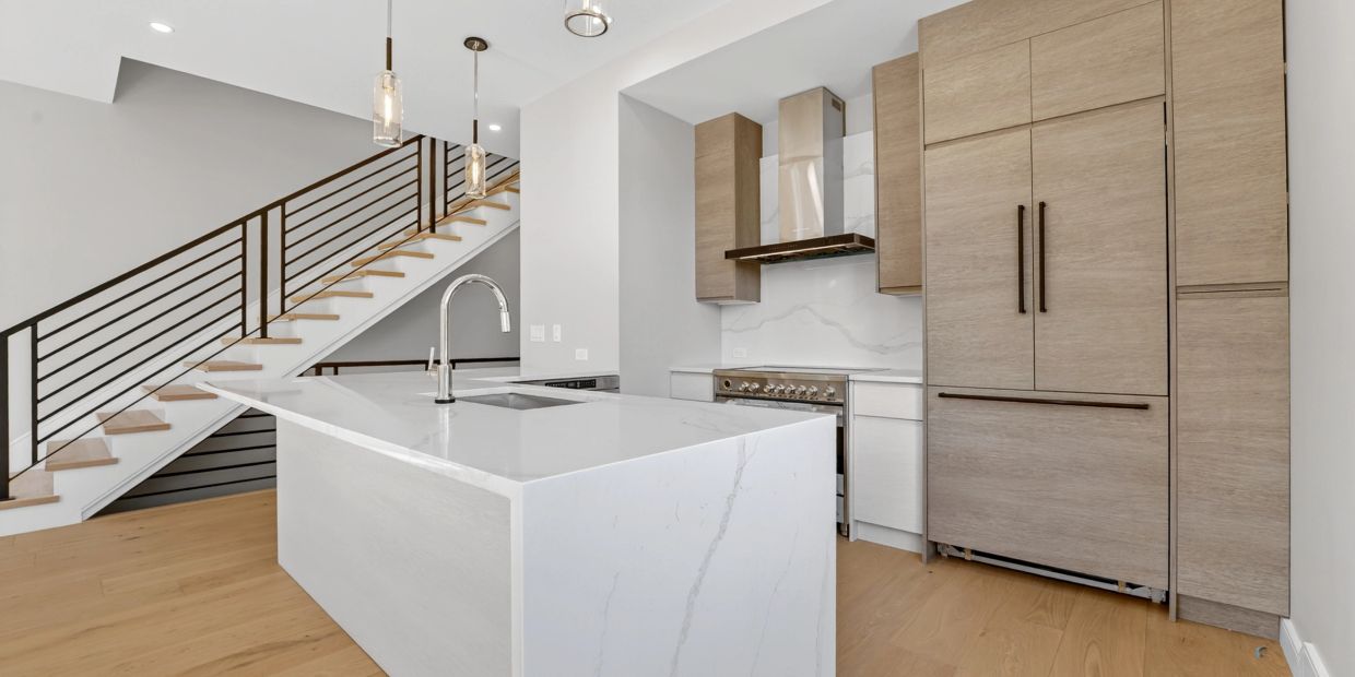 Modern kitchen with marble island and wooden cabinetry near staircase.