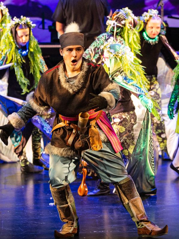 Performer in traditional fur-trimmed costume dancing on stage.