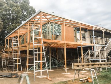 Wooden house frame under construction with ladders around.