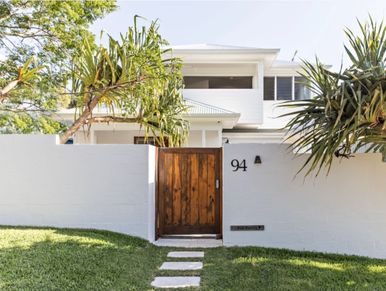 White house with wooden gate and green plants.