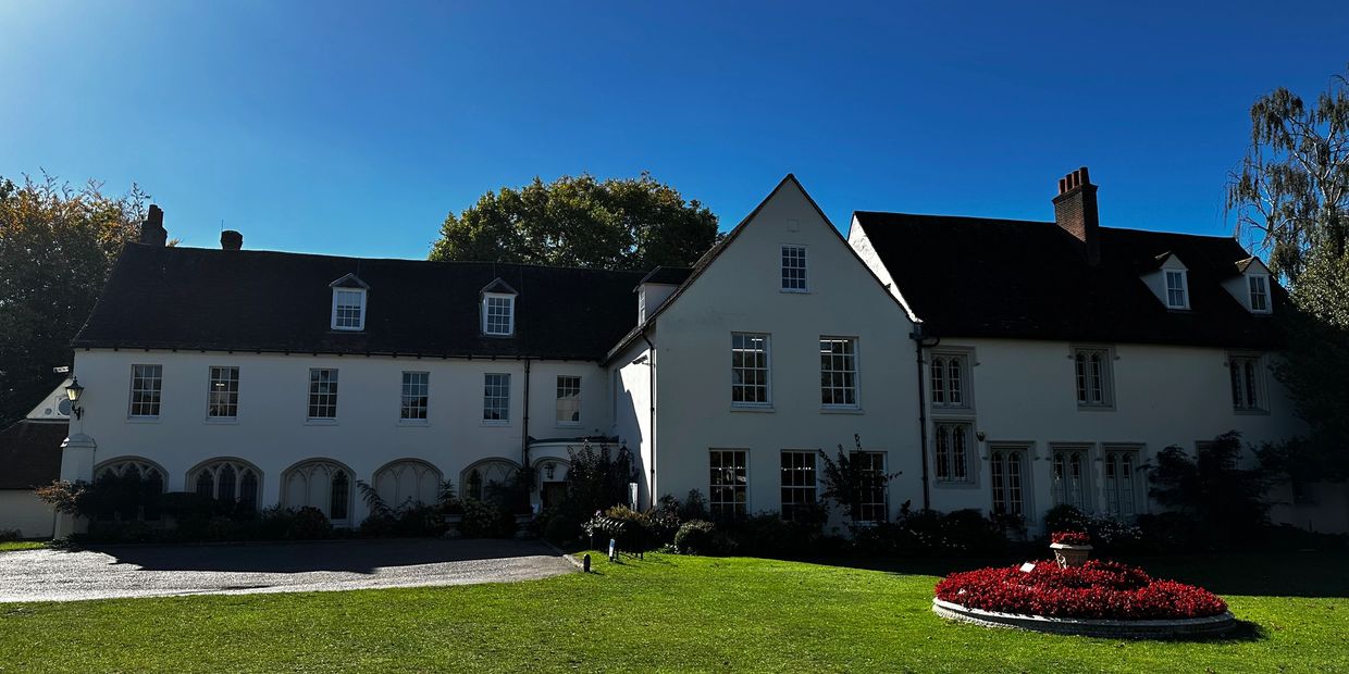 Large white house with dark roof under clear blue sky and green lawn.