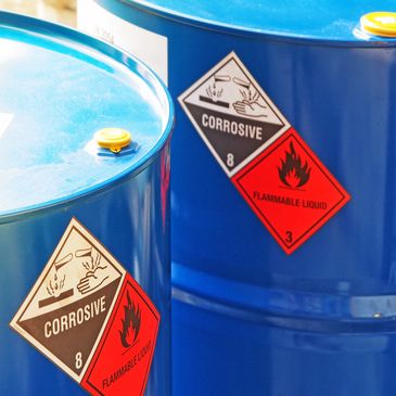 Blue barrels with corrosive and flammable liquid warning labels.