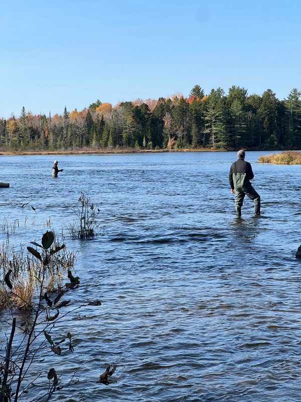 Two men fishing in a lake surrounded by autumn trees.