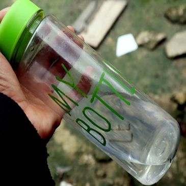 Hand holding a clear water bottle with green cap and text MY BOTTLE.