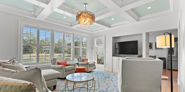 Coffered ceiling living room with lagoon view through plantation shutters. Cozy chairs around a TV