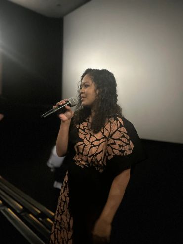 A woman speaking into a microphone in a dimly lit room.