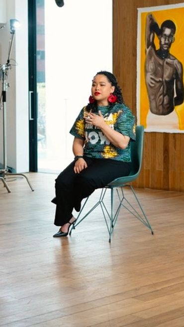 Woman seated in a studio with artwork behind her.