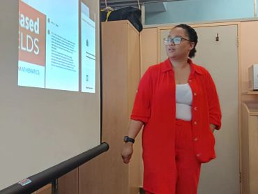 A woman in a red outfit presenting slides in a classroom.