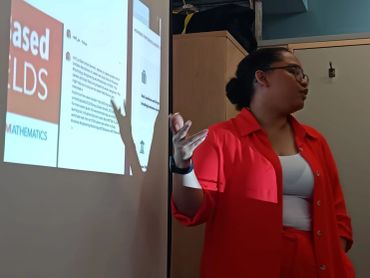 A woman in a red shirt presenting information on a projected screen.