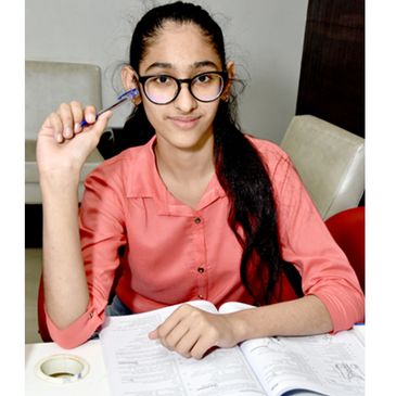 Young woman studying with a pen and book, wearing glasses and a coral shirt.