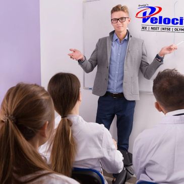 A teacher explaining concepts to students in a classroom at Pooja's Velocity coaching center.