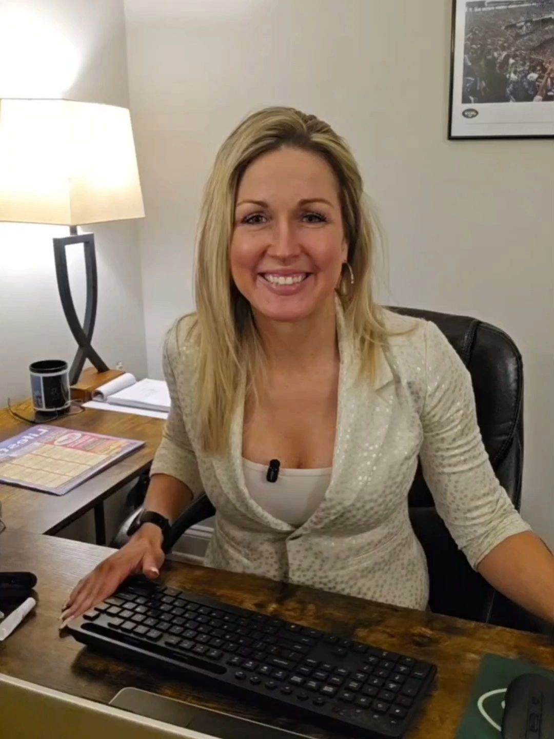 Smiling woman sitting at a desk with a keyboard and laptop.