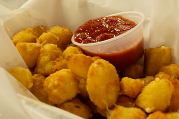 Golden fried hush puppies served with a cup of marinara sauce.