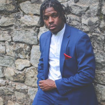 Man in blue suit posing against stone wall.