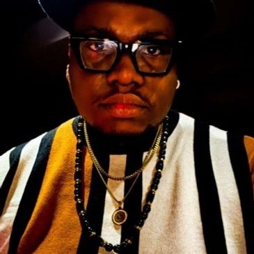 Portrait of a man wearing glasses and layered necklaces.