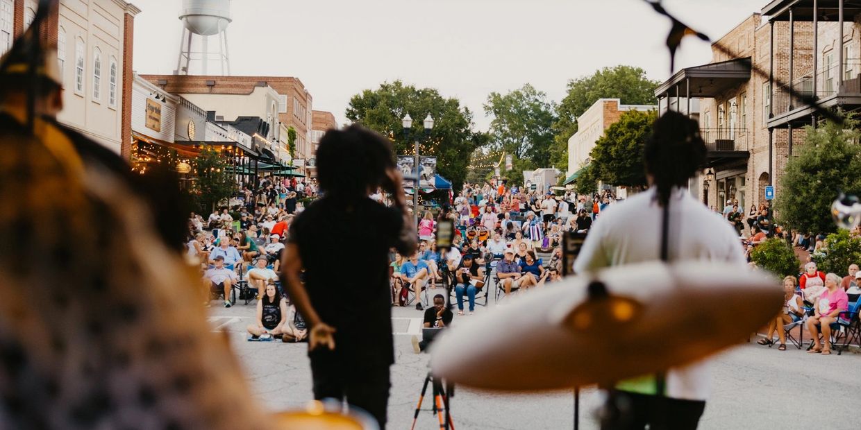 Band performing on street with large audience seated and standing.