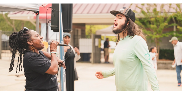 Two people passionately singing outdoors at a casual event.