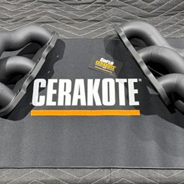 Two black exhaust manifolds on a Cerakote branded mat.