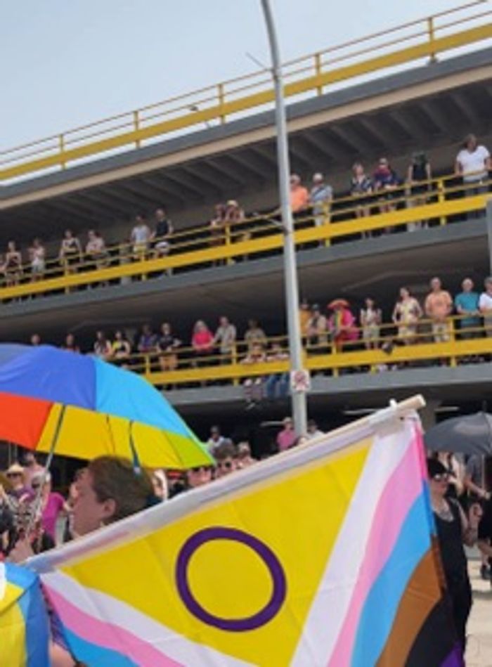 Crowd at a pride event with a nonbinary pride flag and colorful umbrella.