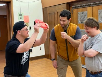 Three men engage in a playful indoor activity using a red frisbee.