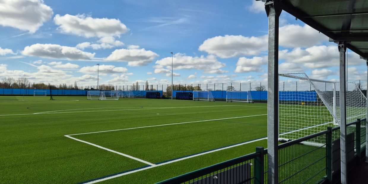 Empty soccer field under a bright, partly cloudy sky.