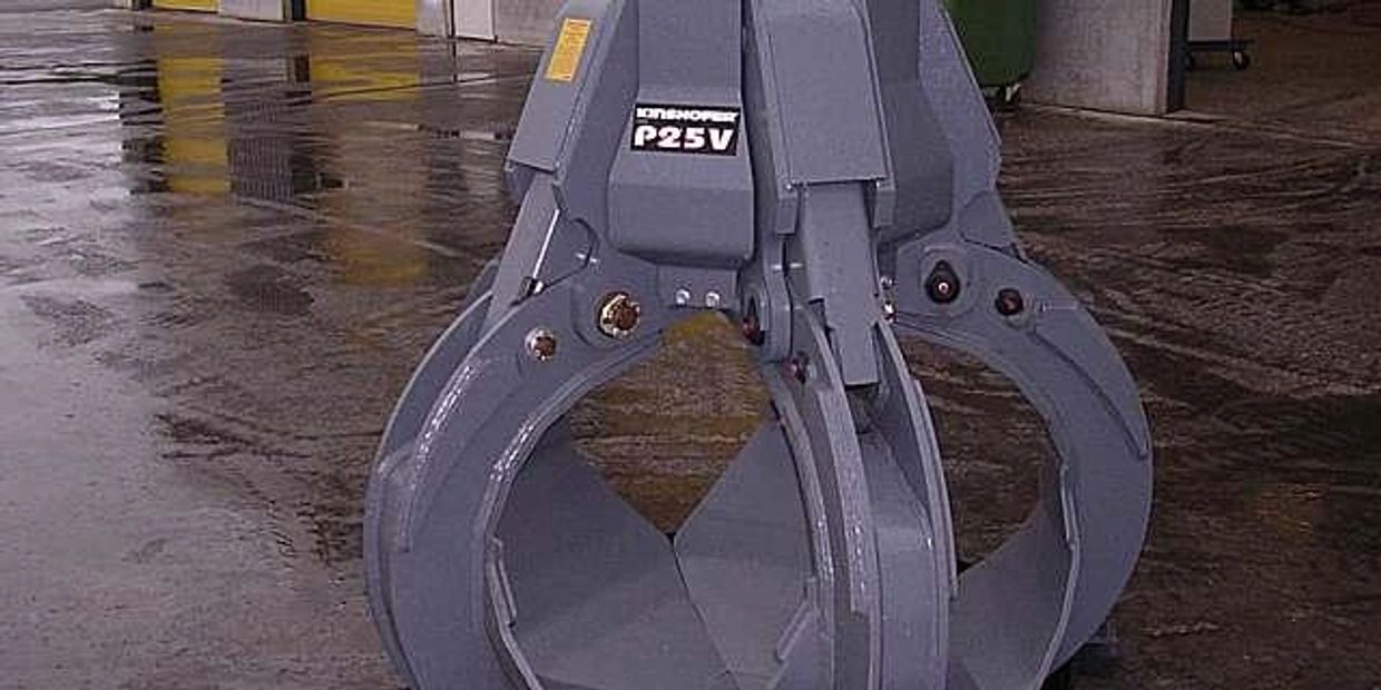 A large industrial grapple attachment labeled P25V on a wet concrete floor.