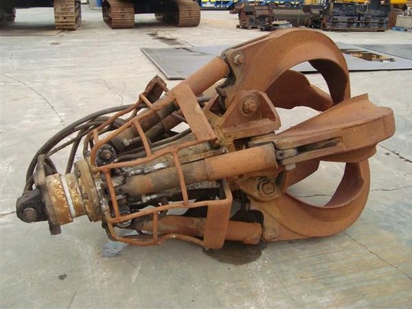 Rusty industrial hydraulic grapple attachment on concrete floor.