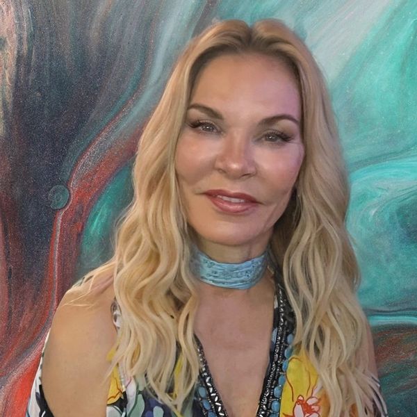 Woman with long blonde hair smiling in front of a colorful background.