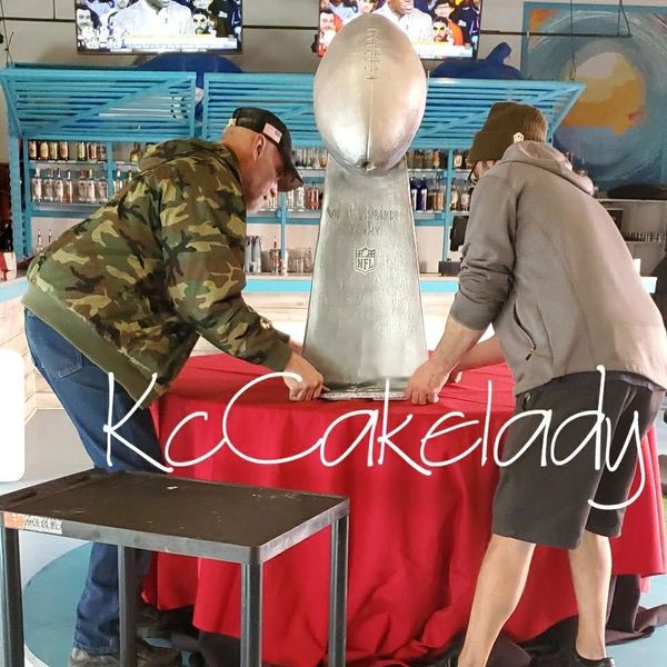 Two men setting up a large NFL Vince Lombardi Trophy replica.