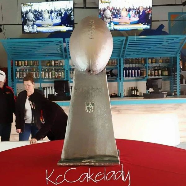 A cake designed like the Vince Lombardi NFL trophy on a red table.