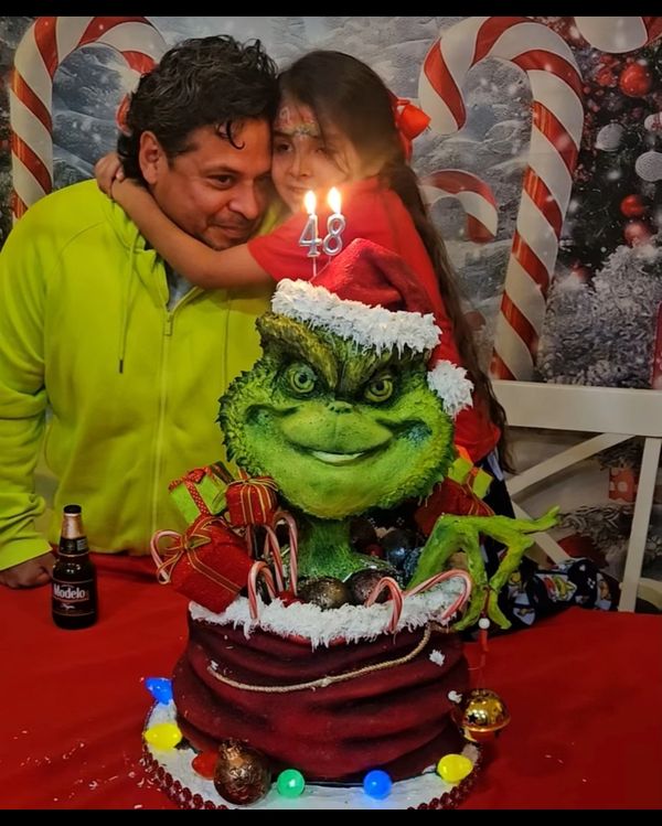 A man and child hug behind a Grinch-themed birthday cake with candles showing 48.