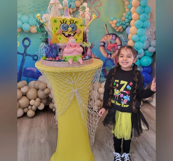 A smiling girl poses next to a SpongeBob-themed birthday cake and colorful balloons.
