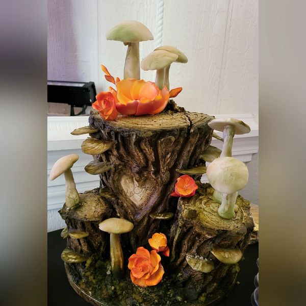 A cake designed like a tree stump with mushrooms and orange flowers.