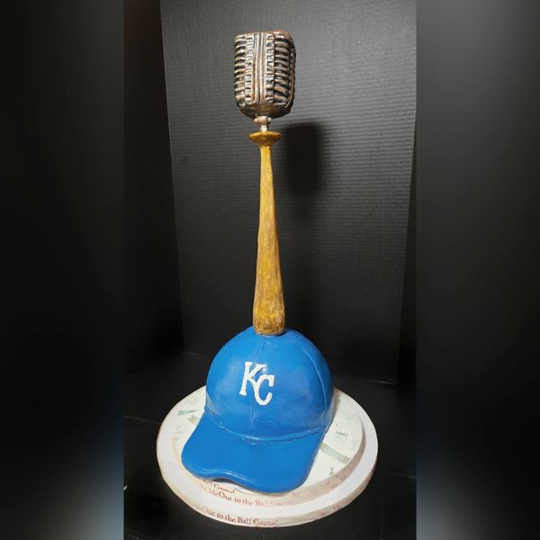 A blue KC baseball cap with a golden microphone trophy on top.