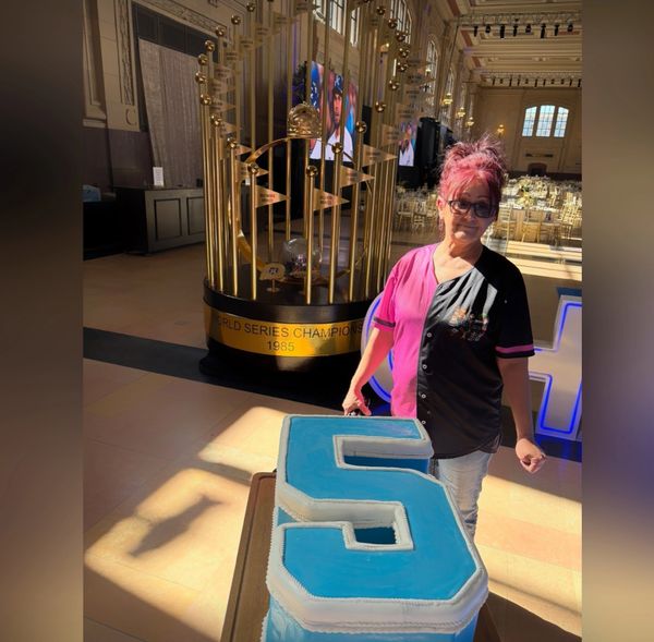 Woman posing with a large blue number 5 cake in a decorated hall.