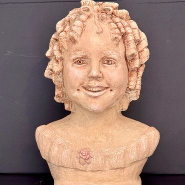 Sculpted bust of a smiling child with curly hair and a flower on the chest.