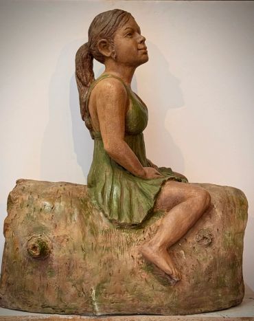 Sculpture of a girl in a green dress sitting on a log.