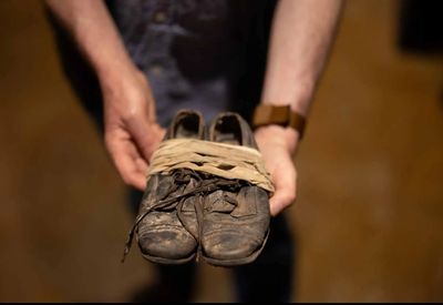 Hands holding old, tied-up worn-out shoes.