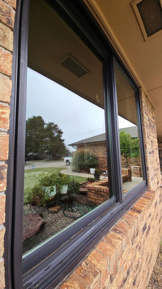 Reflection of garden and house in a large window on a brick wall.