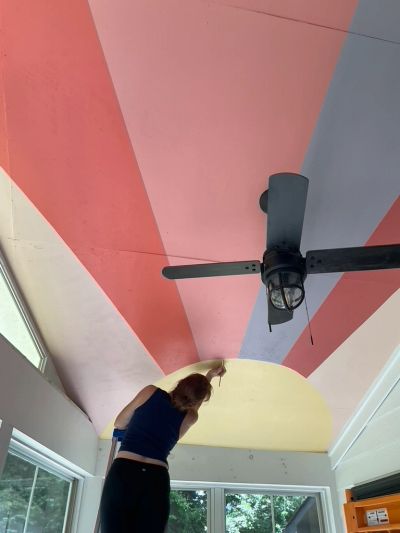 Person painting a colorful ceiling with fan installed.