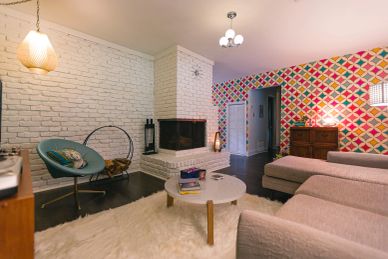 Cozy living room with colorful geometric wallpaper and white brick fireplace.