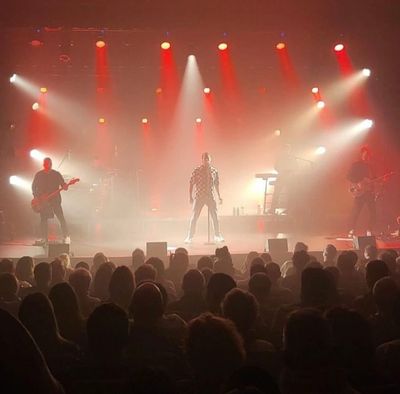 A band performing live on stage with dramatic red and white lighting.